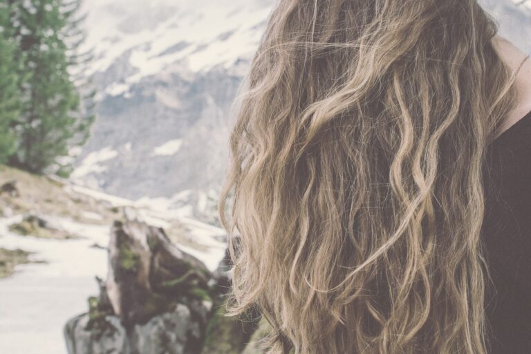 毛先が明るいブラウンのウェーブヘアの寄り。奥に雪の残る山