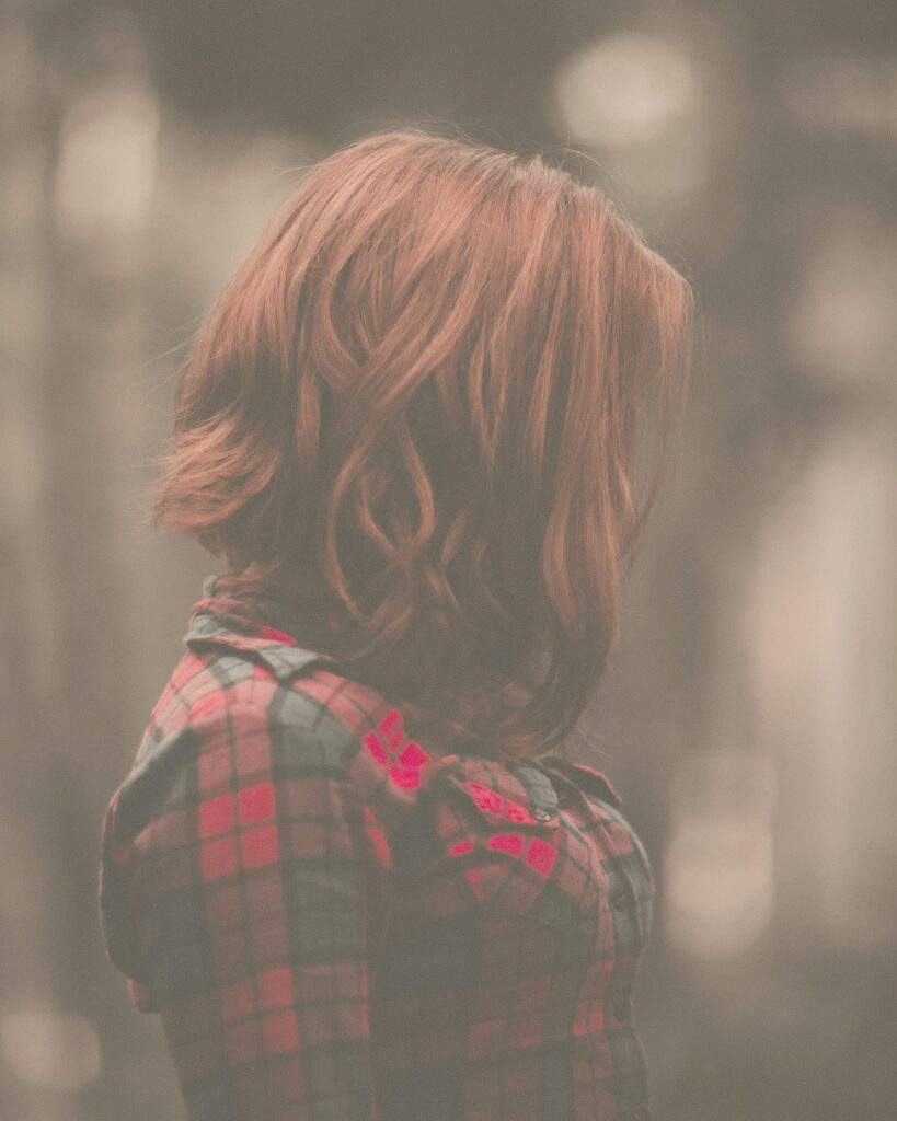 赤みのあるブラウンの、あご下の長さのボブ。チェックのシャツを着た女性の後ろ姿